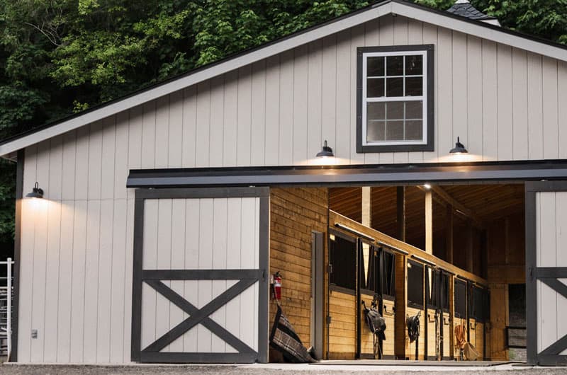 Open barn doors reveal lit stalls with saddles and tack hanging inside