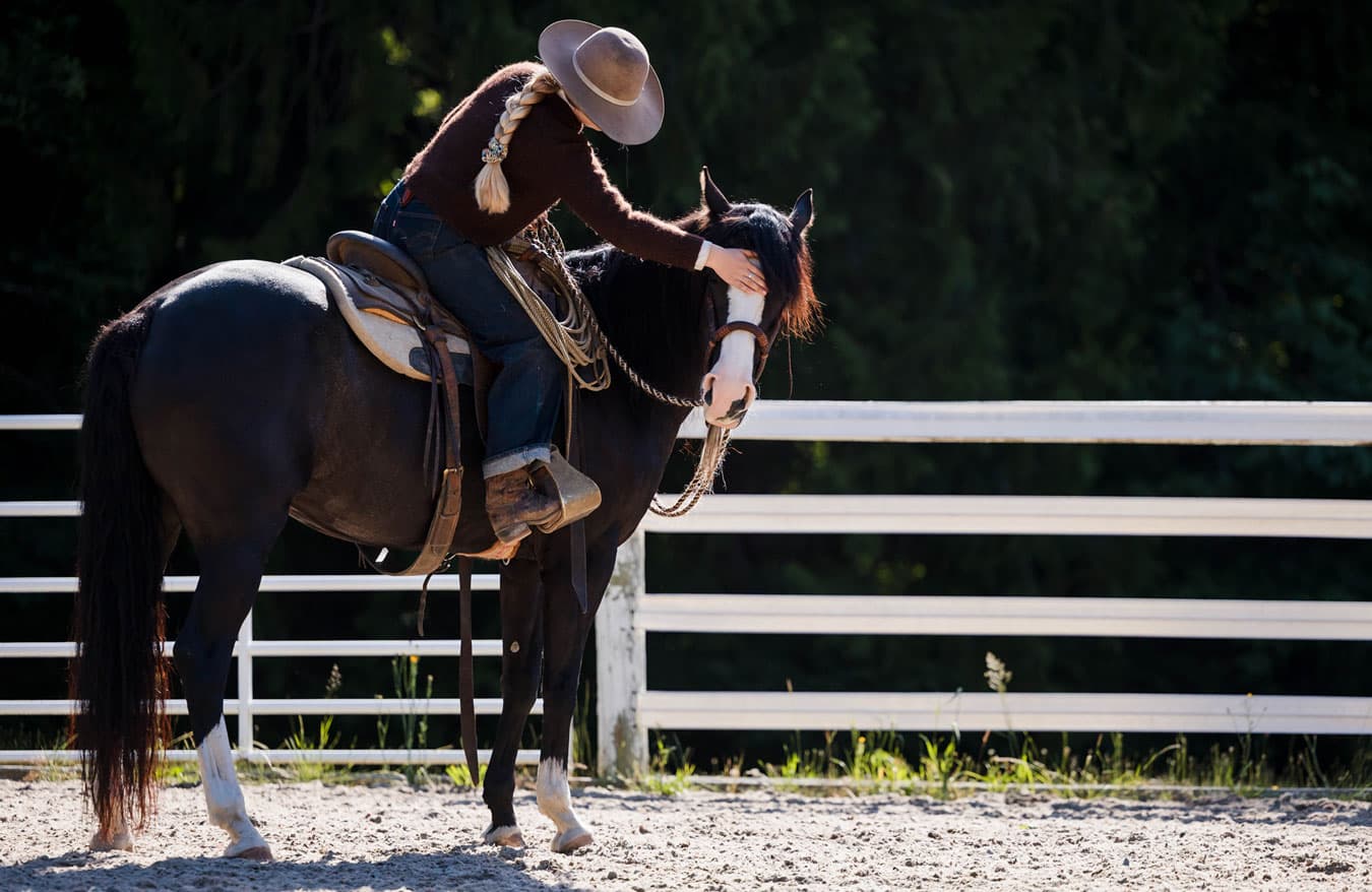 Lili, seated in the saddle, gently pets her horse's head